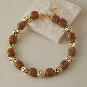 Dettaglio di perline in resina marmorizzata marrone e perle dorate su una collana chic