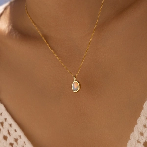 Detailed view of an oval moonstone pendant on a gold chain worn with a white crochet top