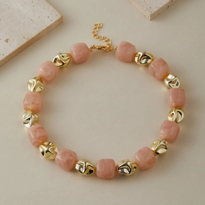 Dettaglio di una collana con perle in resina marmorizzata rosa e grani dorati irregolari