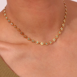 Close-up of a gold necklace with blue floral charms on a model's neck