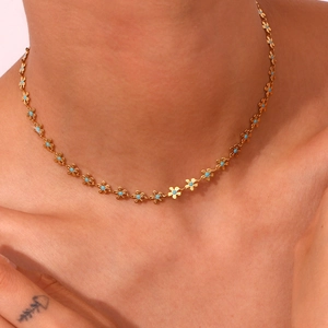 Close-up of gold chain necklace with blue floral charms on woman neck