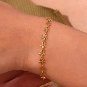 Detailed close-up of a gold floral bracelet with blue beads on a woman wrist