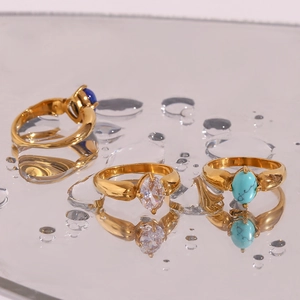 Detailansicht von drei 18K vergoldeten Ringen mit blauen und grünen Edelsteinen auf Wassertropfen