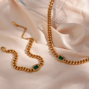Detail of gold Cuban chain jewelry set featuring emerald-cut green stone and pavé accents