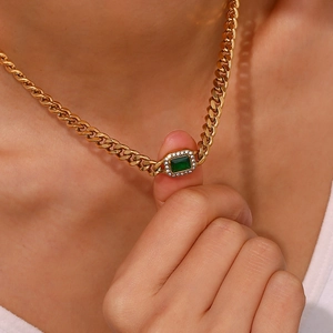 Close-up of golden Cuban link necklace with emerald green gemstone and zircon halo