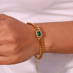 Detailed shot of a gold Cuban chain bracelet with a green rectangular gemstone on wrist