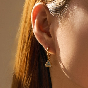 Detail eines 18K vergoldeten Ohrrings mit einem funkelnden Evil-Eye-Dreiecksanhänger