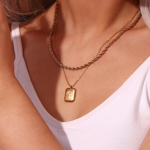 Close-up of a double-layered gold necklace with a square floral embossed pendant on model