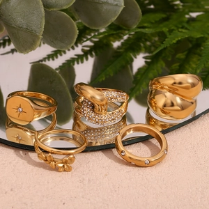 Set of five gold flower and star rings displayed with green plants and a mirror