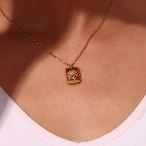 Macro detail of a gold rectangular floral embossed pendant necklace on a model's neck