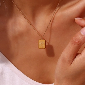 Close-up of gold rectangular floral embossed pendant necklace worn by a woman