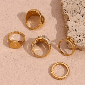 Detailed set of 5 18K gold plated rings with floral and north star patterns on sand stone
