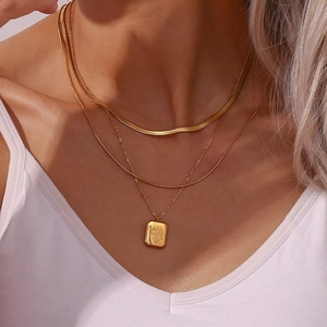 Close-up of triple layered gold necklace featuring rectangular floral pendant and snake chains