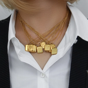 Close-up of stacked gold necklaces featuring square flower embossed pendants on a model