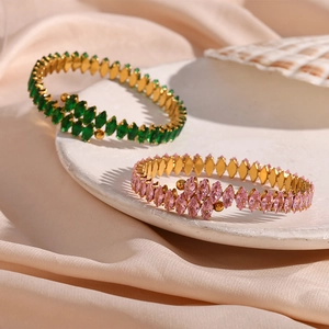 Detailed macro of gold-plated open bracelets with marquise-cut green and pink zircon gems