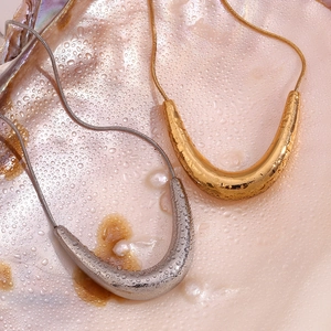Close-up of gold and silver V-shaped pendants on snake chains with elegant water droplets