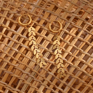 Detail of 18K gold-plated long leaf drop earrings on a textured woven background