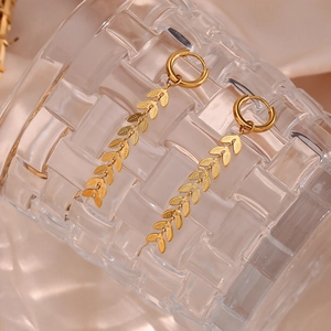 Detailed macro of 18K gold-plated leaf chain drop earrings on a glass rim