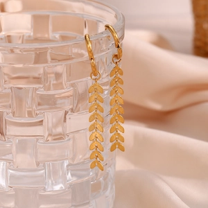 Detail of 18K gold plated long leaf earrings with brushed metal texture hanging on glass