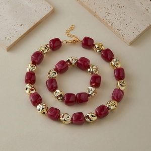 Dettaglio del set collana e bracciale con perle acriliche marmorizzate rosse e dorate