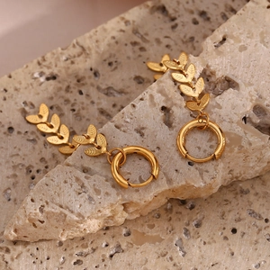 Detailed macro view of 18K gold leaf-shaped huggie earrings on textured stone
