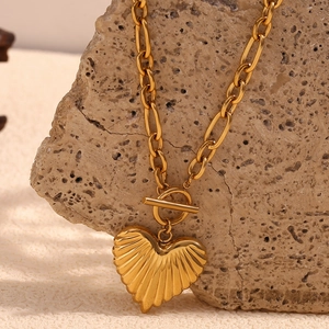 Detail of 18K gold-plated heart pendant on toggle chain draped over natural rock
