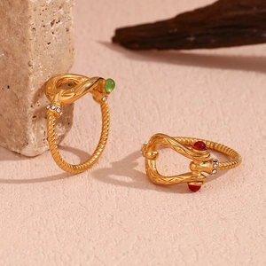 Detail of 18K gold-plated wave rings with green and red gemstones on a natural stone base