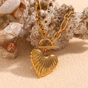 Close-up of 18K gold heart pendant with shell texture and OT toggle clasp on rocks