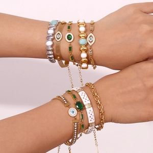 Nahaufnahme von vergoldeten Evil-Eye-Armbändern mit smaragdgrünen Steinen am Handgelenk