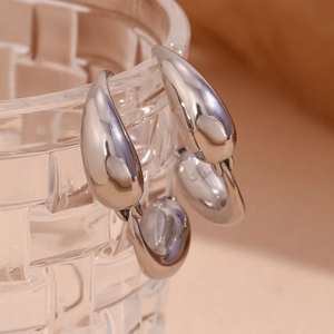 Close-up of polished silver teardrop hoop earrings hanging on a textured glass rim