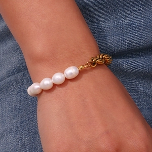 Detail of baroque pearl and gold rope chain bracelet styled on blue denim fabric