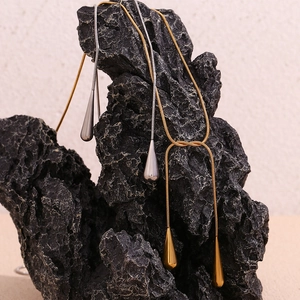 Détail de colliers en maille serpent dorée et argentée avec pendentifs goutte d'eau