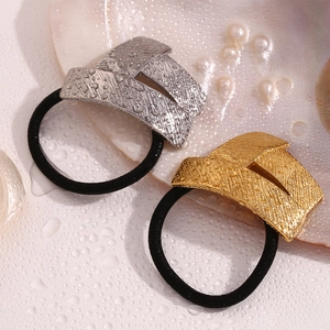 Detailed view of gold and silver wing hair ties with brushed metal texture and water droplets