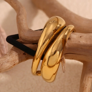 Detail shot of the golden water drop metal piece on a black elastic hair tie on wood