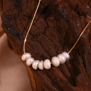 Primer plano de collar chapado en oro 18K con ocho perlas naturales sobre madera oscura
