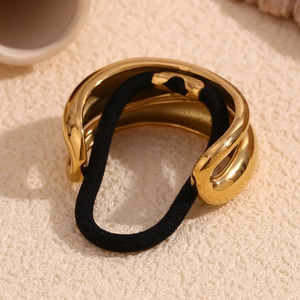 Close-up of golden streamlined twisted metal decoration on black elastic hair tie