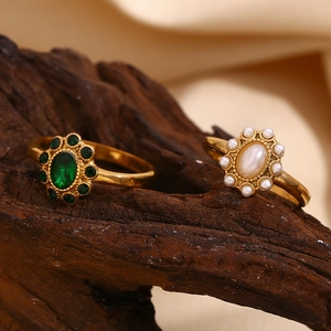 Detailed close-up of 18K gold plated rings with emerald and pearl on dark wood