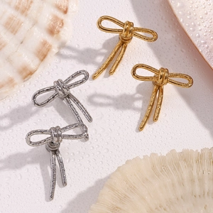 Detail of elegant gold and silver bow stud earrings with textured finish on aquatic background