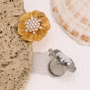 Close-up of gold and silver floral rings with tiny pearls and brushed metal texture