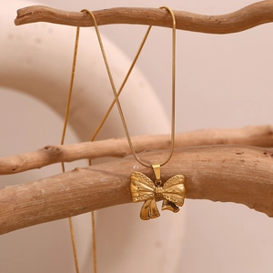 Détail d'un pendentif nœud en or 18K sur une chaîne serpent fine posée sur une branche