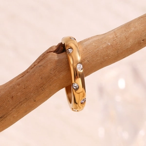 Detailansicht eines vergoldeten Dome-Rings mit Zirkonia-Steinen auf einem Holzzweig