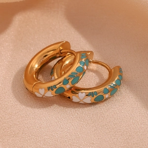 Detailopname van 18K vergulde oorringen met witte emaille bloemen en blauw patroon