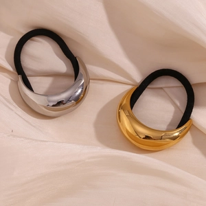 Detailansicht mondförmiger Gold- und Silber-Haargummis auf elegantem cremefarbenem Seidenstoff