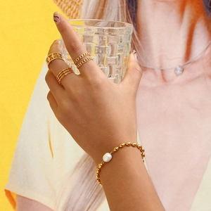 Detailed view of gold rings and pearl bracelet worn while holding a glass cup
