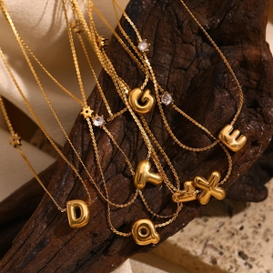 Dettaglio macro di collane con lettere a bolla placcate in oro 18K con zirconi su seta