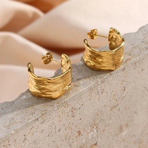 Macro view of C-shaped earrings with textured golden finish on stone surface
