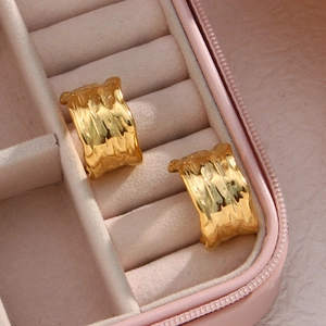 Macro detail of 18K gold plated C-shaped earrings with irregular hammered texture on velvet