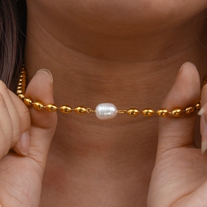 Detailed close-up of a golden oval bead necklace featuring a central white baroque pearl