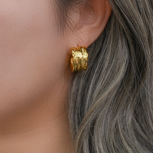 Close-up of model wearing gold hammered C-shape earrings with irregular lava texture
