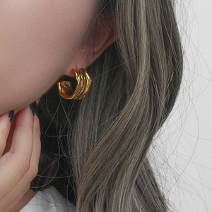 Detail of 18K gold-plated C-shape hoop earrings with hammered lava texture on a model